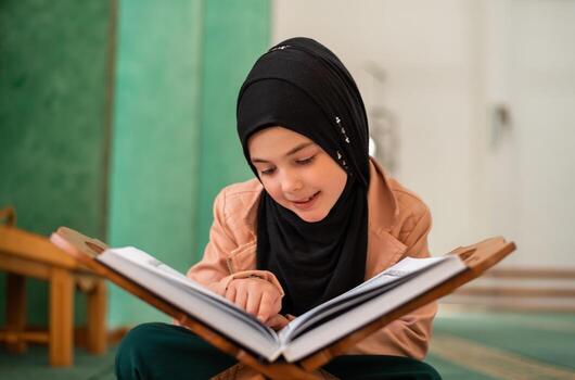 a muslim kid girl reading a quran inside the mosque photo